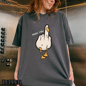 May include: A dark gray t-shirt with a white cartoon goose giving the middle finger. The text "Duck You" is printed above the goose.