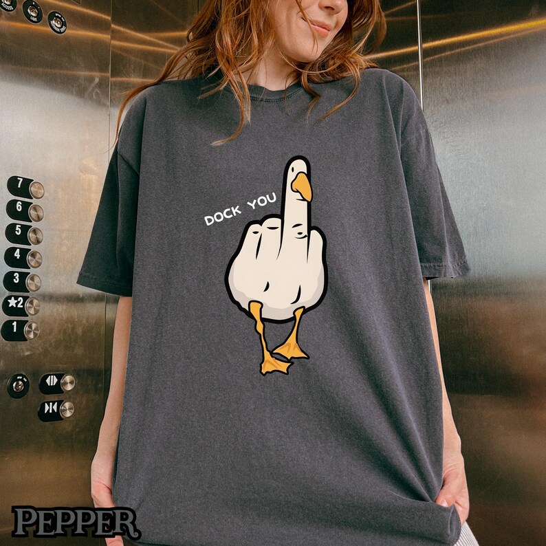 May include: A dark gray t-shirt with a white cartoon goose giving the middle finger. The text "Duck You" is printed above the goose.