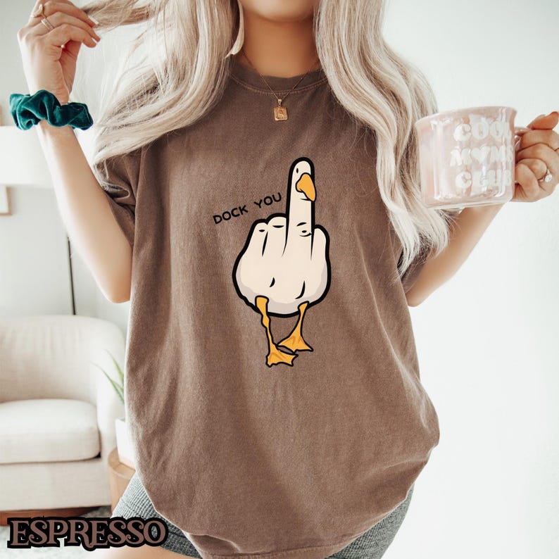 May include: A brown t-shirt with a cartoon duck giving the middle finger. The text "Duck You" is printed on the shirt.