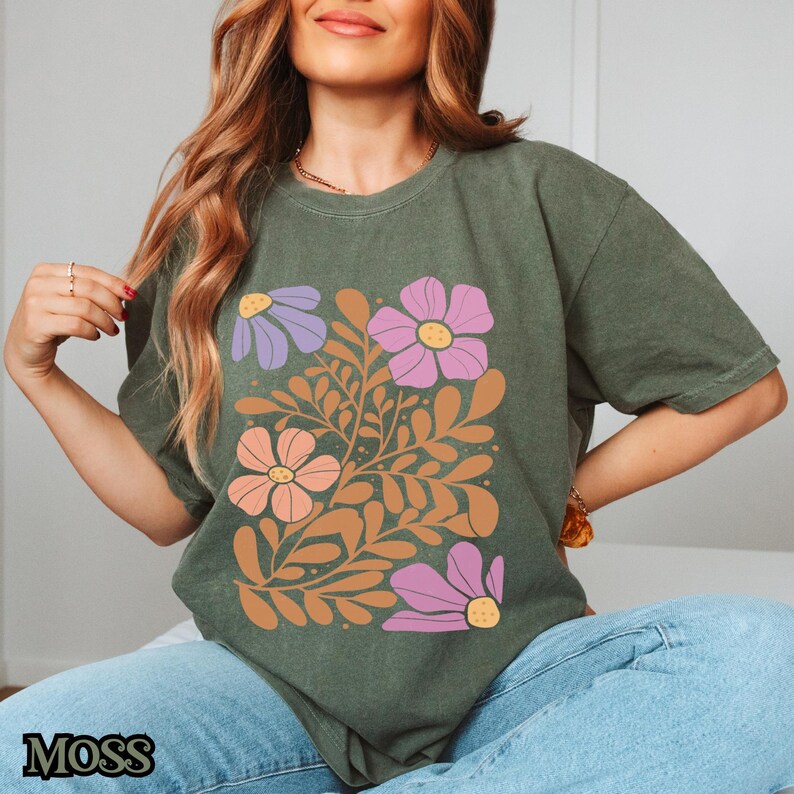 Op de afbeelding: Een groen T-shirt met een bloemenprint met roze, paarse en oranje bloemen met bruine stelen en bladeren.