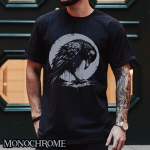 May include: Black t-shirt with a graphic of a crow in a circle. The crow is black and white and has a dripping effect. The text "MONOCHROME" is at the bottom of the shirt.