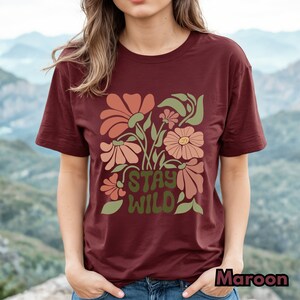 May include: A maroon t-shirt with a floral design and the text "Stay Wild" in green letters.