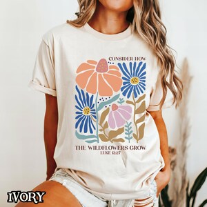 May include: A beige t-shirt with a floral design and the text "Consider how the wildflowers grow Luke 12:27".