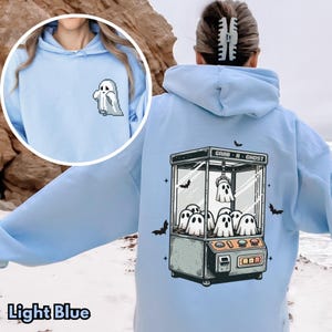 Pode incluir: Moletom azul claro com um gr&aacute;fico de m&aacute;quina de garra fantasma nas costas e um fantasma pixelado na frente. O texto na m&aacute;quina de garra diz "Grab-A-Ghost".