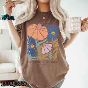 May include: Brown t-shirt with a floral design and the text "Consider the lilies how they grow..." and "The wildflowers grow... Luke 12:27".