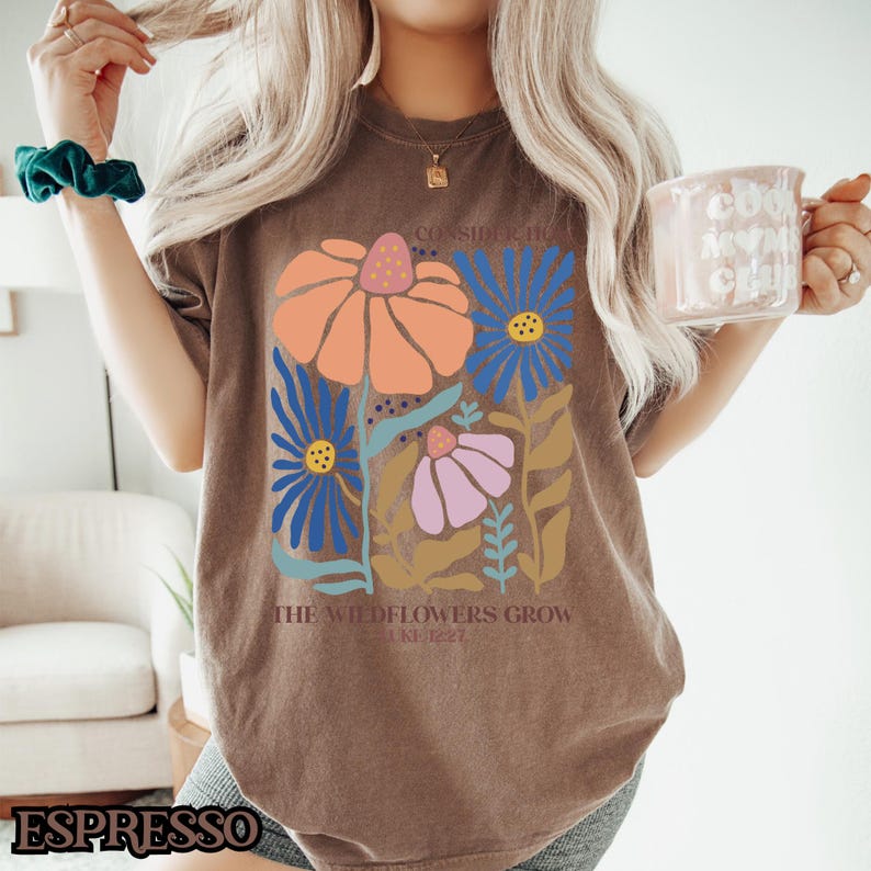 May include: Brown t-shirt with a floral design and the text "Consider the lilies how they grow..." and "The wildflowers grow... Luke 12:27".