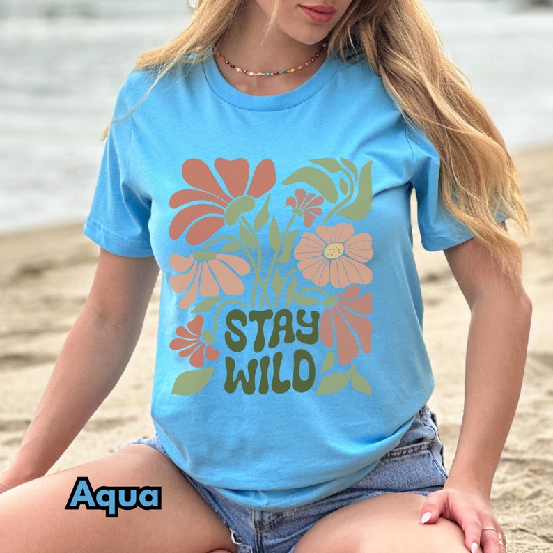 May include: A light blue t-shirt with a floral design and the text "Stay Wild" in a retro font.