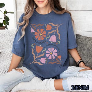 Pu&ograve; includere: Una maglietta blu navy con un design floreale e il testo "Life is a balance of holding on and letting go".