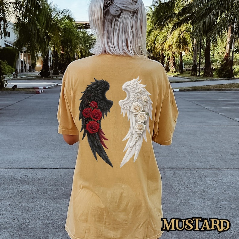 May include: A mustard yellow t-shirt with a black and white angel wing design. The wings are on the back of the shirt and are surrounded by red roses.