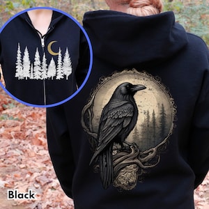 Puede incluir: Sudadera con capucha negra con un estampado gráfico de un cuervo posado en una rama en un entorno de bosque. El cuervo es negro con un pico amarillo y el bosque está representado en tonos grises y marrones. La luna es una media luna y es amarilla.