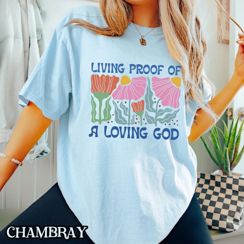 May include: Light blue t-shirt with a floral design and the text "Living Proof of a Loving God".