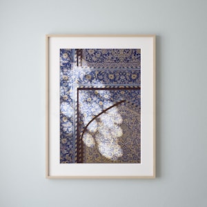 Könnte beinhalten: Nahaufnahme eines blauen und goldenen Fliesenbogens mit komplizierten floralen Mustern. Sonnenlicht scheint durch den Bogen und wirft Schatten auf die Fliesen.