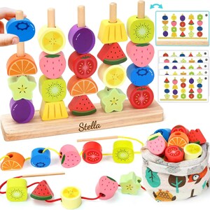 May include: Wooden fruit-shaped bead set with a wooden base and pegs. The beads include various fruits like strawberries, kiwis, and oranges. The set includes a drawstring bag and pattern cards for matching. The base is engraved with the name "Stella".