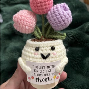 May include: A handmade crochet flower pot with three colorful tulips. The pot is white with a smiling face and a message that reads "IT DOESN'T MATTER HOW OLD I GET, I ALWAYS NEED YOU Mom."