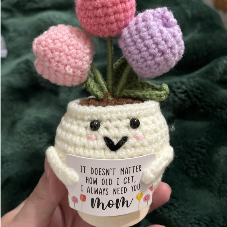 May include: A handmade crochet flower pot with three colorful tulips. The pot is white with a smiling face and a message that reads "IT DOESN'T MATTER HOW OLD I GET, I ALWAYS NEED YOU Mom."