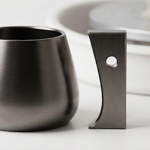 May include: A dark metallic pottery rib tool labeled PR1, featuring a smooth, curved, bowl-like shape and a separate vertical handle component with a small circular hole, presented together as a set for ceramic shaping and smoothing tasks.