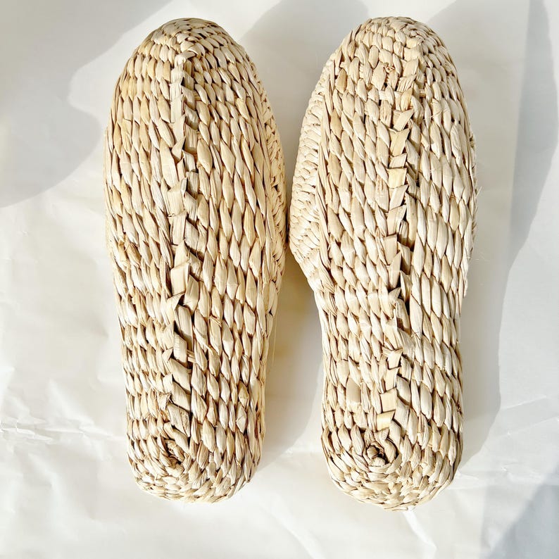 May include: A pair of natural woven straw slippers. The slippers are beige and have a woven pattern.