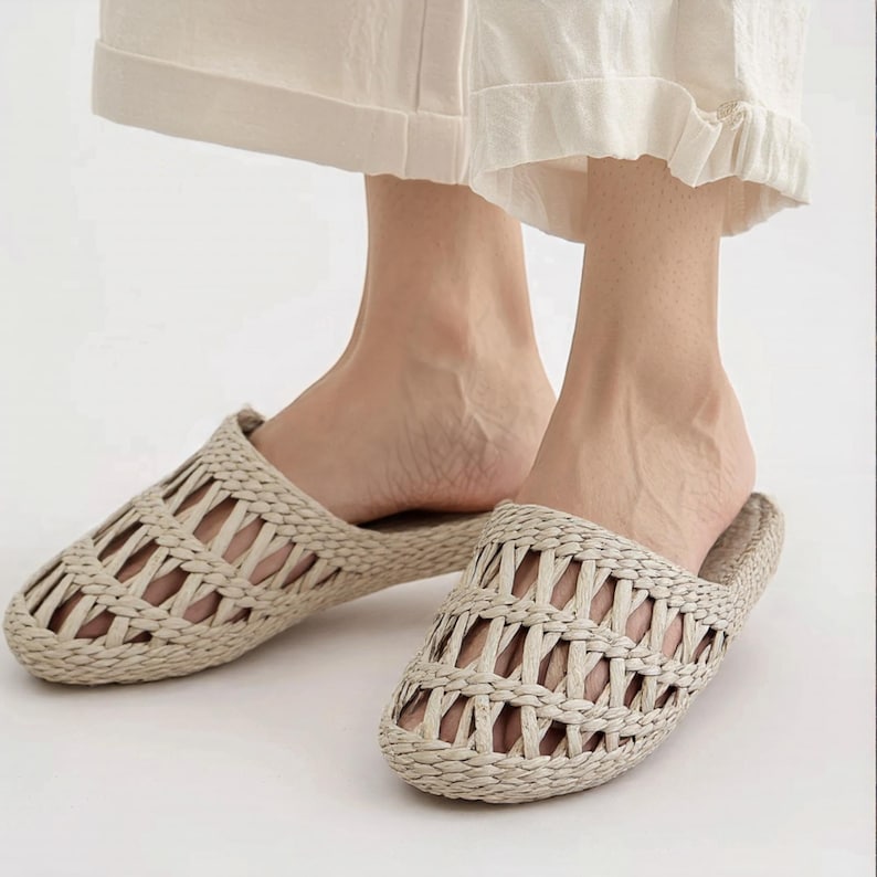 Woman wearing woven straw slippers with open-weave braided uppers and flat natural soles. Lightweight, breathable, and eco-friendly design, ideal for summer beach wear or casual indoor comfort.