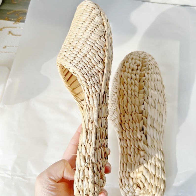 May include: A pair of woven straw slippers. The slippers are beige and have a simple design.