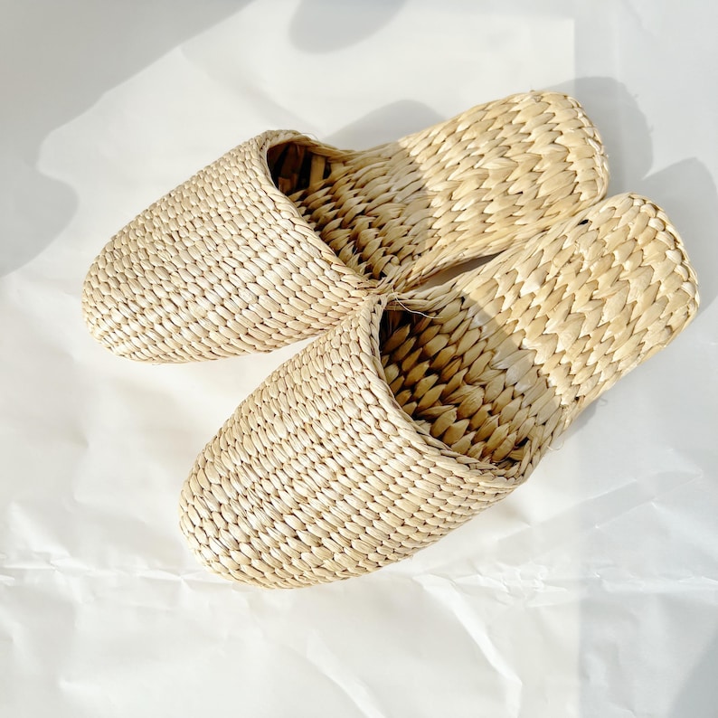 May include: A pair of woven straw slippers in a light beige color. The slippers are made of a natural material and have a simple, comfortable design.