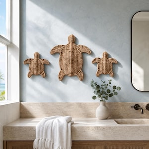 a bathroom with a large mirror, a towel, and a vase with greenery. There are three woven turtle-shaped wall decorations on the wall, and a window can be seen in the background.