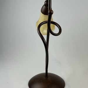 May include: A decorative table lamp with a bronze finish. The lamp features a curved stem and a swirling design element. The lampshade is a teardrop shape with a cream-colored glass. The lamp has a round base and a power cord.