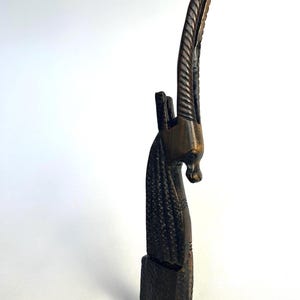 May include: A dark brown, carved wooden sculpture of an antelope. The sculpture features detailed carvings of the antelope's head, long horns, and body. The antelope is standing on a rectangular base. The sculpture is set against a white background.