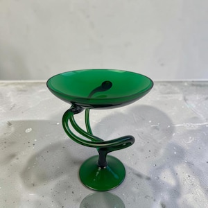 Könnte beinhalten: Eine tief smaragdgrüne Glasschale mit einem breiten, kreisförmigen Becken, das von einem skulpturalen, spiralförmigen Stiel getragen wird, der mit einem soliden, runden Fuß verbunden ist. Das Glas ist durchscheinend und hat eine glatte Oberfläche.