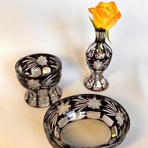 Può includere: Set di tre pezzi di servizio in vetro tagliato. Il set comprende un piccolo vaso con una rosa gialla, una piccola ciotola e una ciotola più grande. Ogni pezzo è rosso scuro con un motivo floreale e accenti trasparenti.