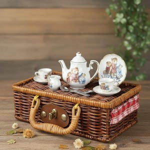 Puede incluir: Un juego de té de porcelana en miniatura con ilustraciones de ositos de peluche, que incluye una tetera, dos tazas con platillos, una jarra de leche y un plato pequeño, dispuestos sobre una cesta de picnic de mimbre trenzado marrón con cierre.