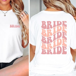 Könnte beinhalten: Weißes T-Shirt mit dem Wort "BRIDE" in Pink auf der Vorderseite und einem sich wiederholenden Muster von "BRIDE" in Pink und Pfirsich auf der Rückseite.