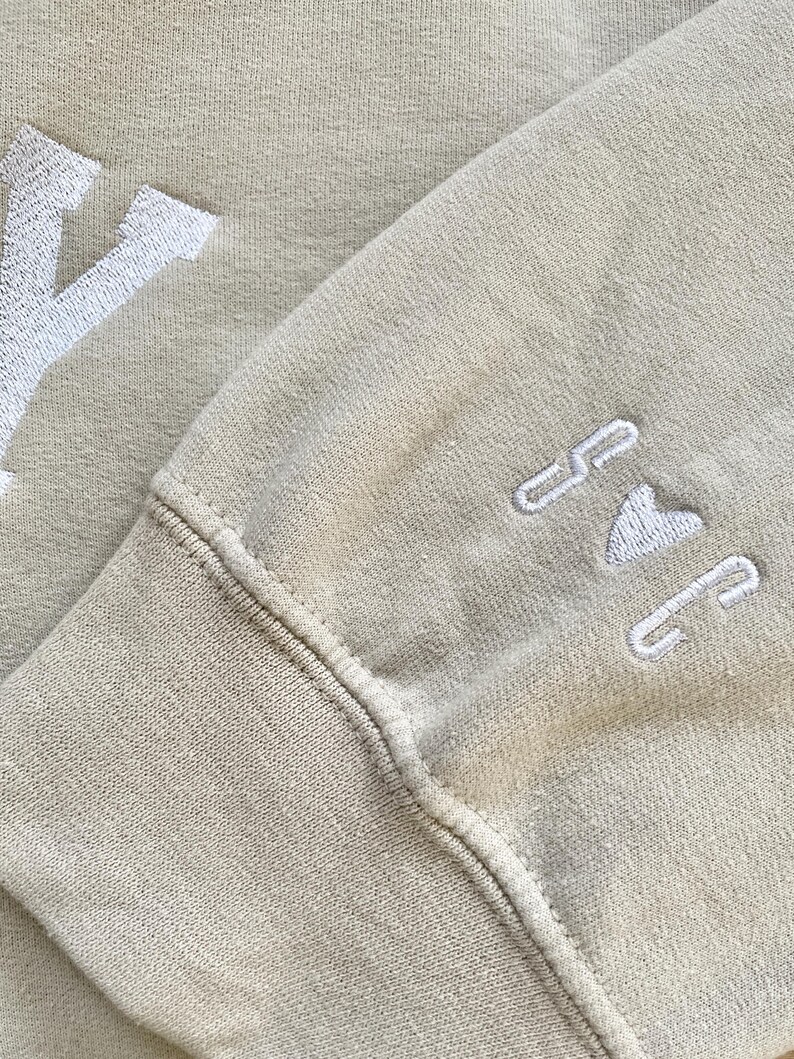 May include: A beige sweatshirt with white embroidered lettering that says "Y" on the left side and "I <3 NY" on the right side.