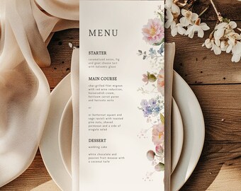 May include: A wedding menu with a floral design. The menu includes a starter, main course, and dessert. The starter is caramelized onion, fig, and goat cheese tart with balsamic glaze. The main course is char-grilled filet mignon with red wine reduction, horseradish cream, heirloom carrot puree, and haricots verts, or butternut squash and sage ravioli with toasted pine nuts, shaved parmesan, and a side of arugula salad. The dessert is wedding cake, white chocolate and passion fruit mousse with a coconut tuile.