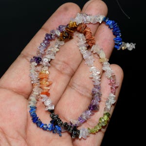 May include: A multi-coloured gemstone chip necklace featuring irregular, tumbled stones in shades of blue, purple, orange, brown, green, and clear white. The small, polished mineral fragments are strung together on a thin, flexible cord.