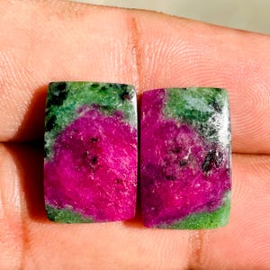 Peut inclure: Deux pierres précieuses rectangulaires avec une palette de couleurs vibrantes. Les pierres présentent une combinaison saisissante de teintes magenta profond et vert émeraude. Le centre magenta est entouré d'une bordure verte, créant un contraste visuellement attrayant. Les pierres sont probablement utilisées pour la bijouterie.