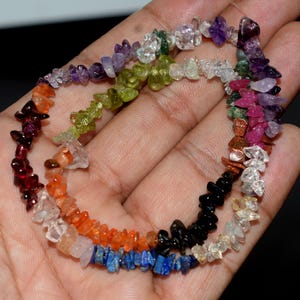 May include: A multi-colored strand of irregular, tumbled gemstone chips featuring a vibrant spectrum of colors including deep purple amethyst, bright green peridot, fiery orange carnelian, dark red garnet, deep blue lapis lazuli, and black onyx.