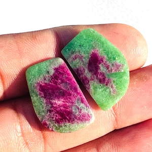 May include: Two polished gemstones with a vibrant colour combination. The stones feature a striking contrast of deep magenta and light green hues. The gemstones are likely used for jewellery or decorative purposes.
