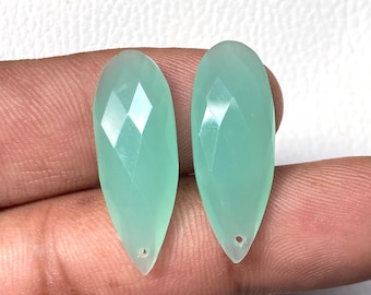 May include: Two faceted, teardrop-shaped gemstones in a pale green hue. Each stone has a small hole at the pointed end, suggesting they are intended for jewelry making. The stones are displayed against a neutral background.