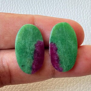 May include: Two oval gemstones with a green and magenta colour scheme. The gemstones have a polished surface and a natural appearance. The green colour dominates the top portion of the stones, while the magenta colour is concentrated in the lower half.