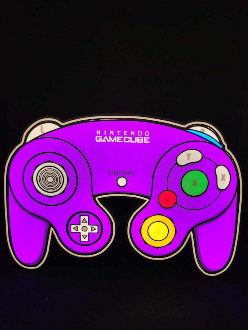 May include: A purple Nintendo GameCube controller with white buttons and a black background. The controller has a circular button in the center, a directional pad, and four face buttons labeled A, B, X, and Y.