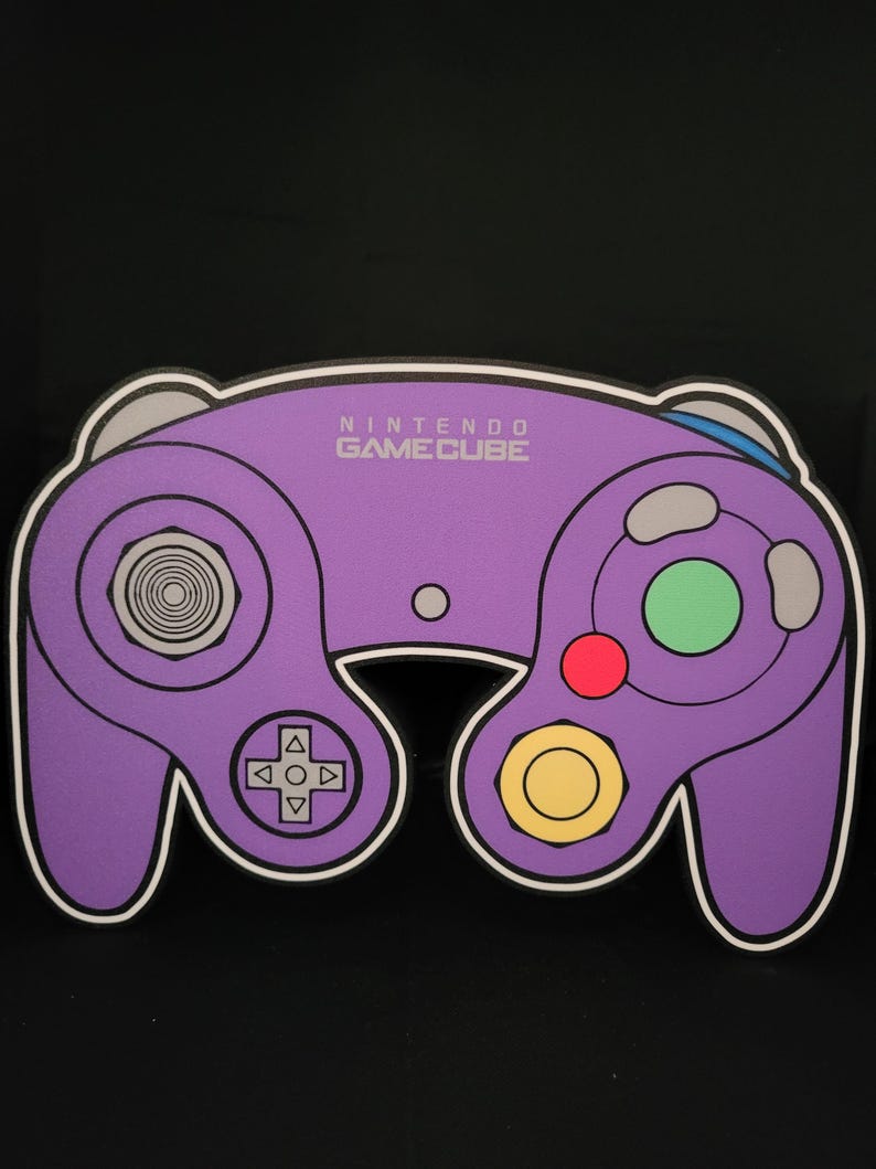 May include: Purple Nintendo GameCube controller with a white outline. The controller has a circular button in the center, a directional pad, and two analog sticks. The text "NINTENDO GAMECUBE" is printed in white on the controller.
