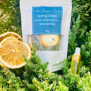 May include: A white pouch with a blue label that reads "Blue Juniper Goods Spring Clean Lemon Rosemary Mint Simmer Pot 30g". The pouch contains dried citrus slices and herbs. A small bottle of essential oil is next to the pouch.