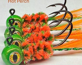 May include: Three fishing lures labeled Hot Perch, each featuring a bright green round head with a large yellow and black eye, a textured orange and green body, and a long curved metal hook with bright orange feathers and green tinsel.