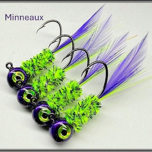 May include: Four fishing lures with purple and green accents. Each lure features a purple head with a yellow eye, a green fuzzy body, and a hook with purple and green feathers. The word "Minneaux" is in the top left corner.
