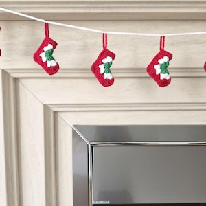 May include: A garland featuring five small crocheted stockings hanging from a white string. Each stocking is crafted with a red outer edge, a white middle section, and a green centre, all suspended by a matching red crocheted loop at the top.