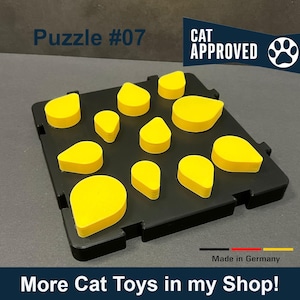 Könnte beinhalten: Ein schwarzes Puzzle-Spielzeug für Katzen mit dem Text "Puzzle #07" und "CAT APPROVED" darauf. Das Puzzle hat 11 gelbe, tropfenförmige Teile, die in das Puzzle passen.