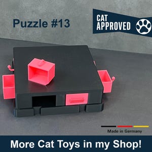 May include: A black cat toy puzzle with pink drawers and a pink lid. The puzzle is labeled "Puzzle #13" and "CAT APPROVED".