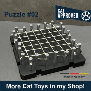 Könnte beinhalten: Ein schwarz-weißes Katzenspielzeug-Puzzle mit einem weißen Schnurgitter und grauen Stangen. Das Puzzle ist mit "Puzzle #02" und "CAT APPROVED" beschriftet. Der Text "Made in Germany" ist ebenfalls sichtbar.