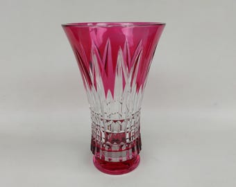 Puede incluir: Un jarrón de cristal transparente con borde y base magenta vibrantes. El jarrón presenta un diseño detallado de cristal tallado con patrones verticales y geométricos. La parte superior es magenta sólido, que pasa a cristal transparente.