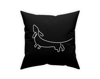 May include: Black throw pillow with a white line drawing of a dachshund on a black background.